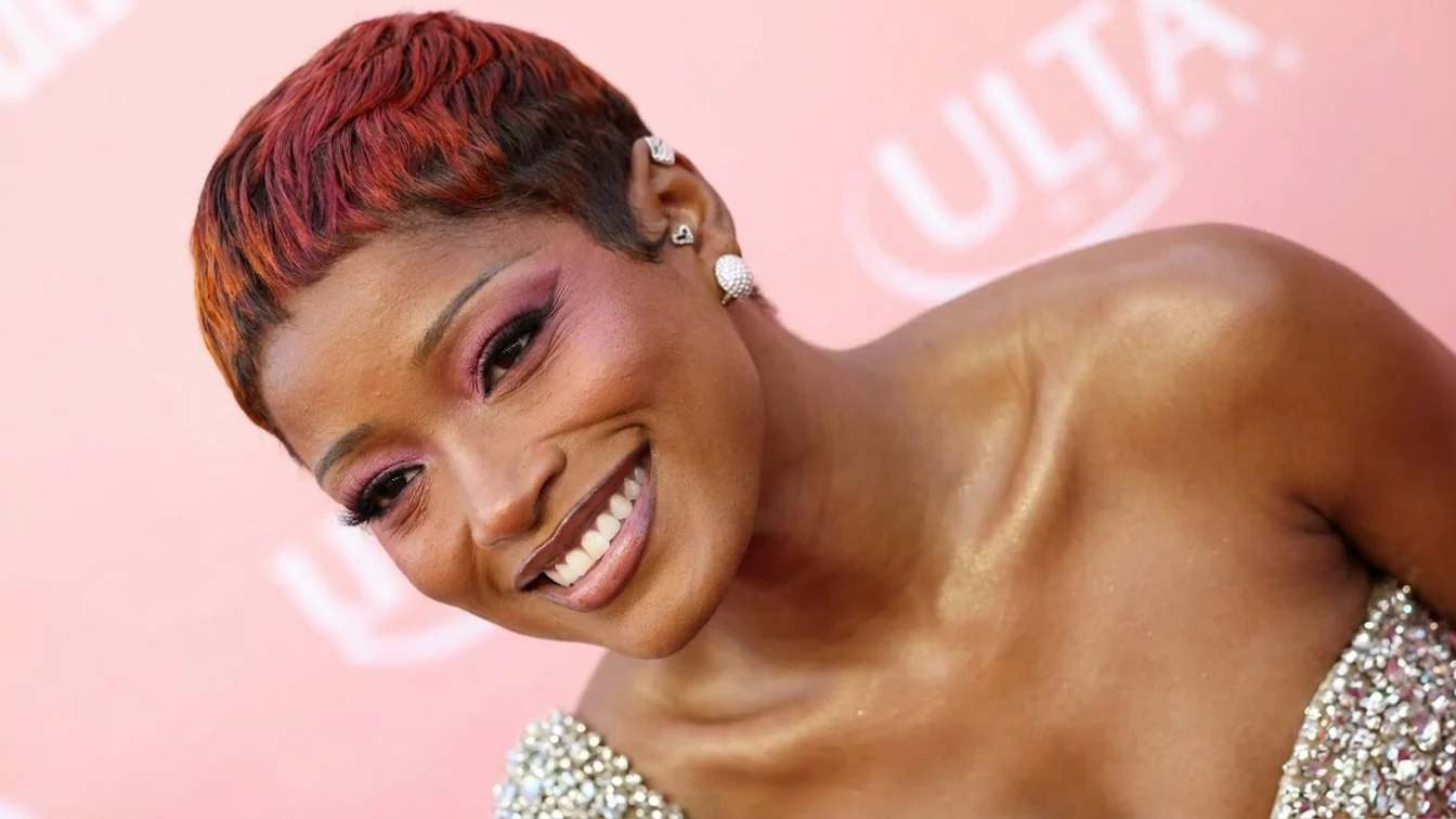 Keke Palmer smiles on the red carpet in pink eye shadow. Her hair is a blend of auburn and strawberry.