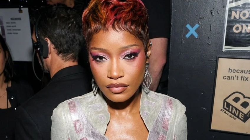 Keke Palmer poses backstage in a silver jacket and pants and pink makeup.