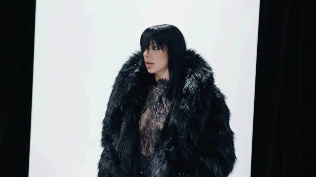 Charli XCX walks the runway in a black fauxfur coat lace top and long hair styled with bangs.