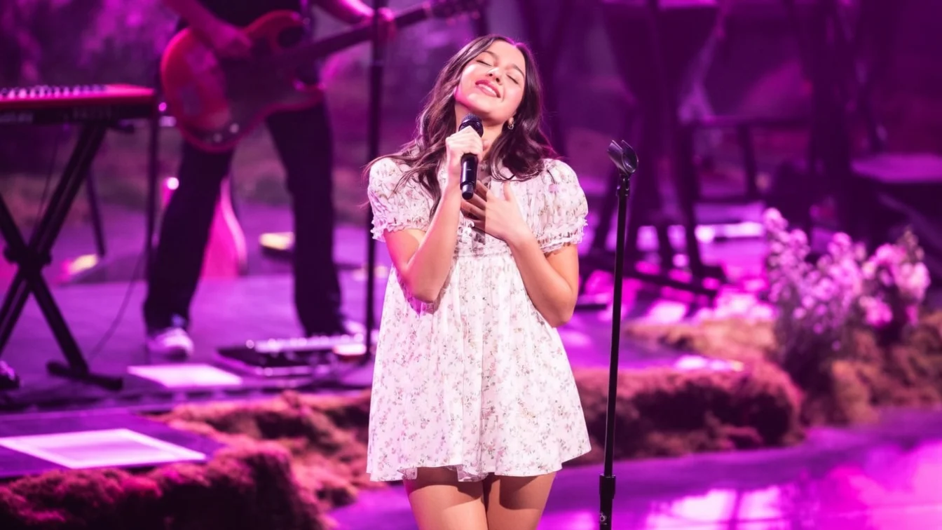 Olivia Rodrigo performing on stage in a babydoll dress that sparked online debate, later prompting the singer to speak out about the sexualisation of girlhood and double standards facing young women.