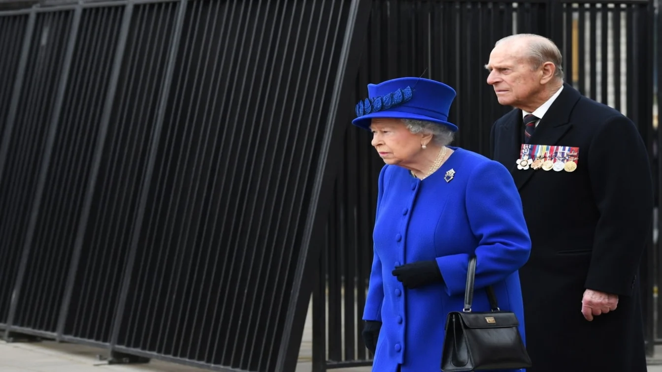 Prince Philip in a black coat walking with the Queen in a blue outfit