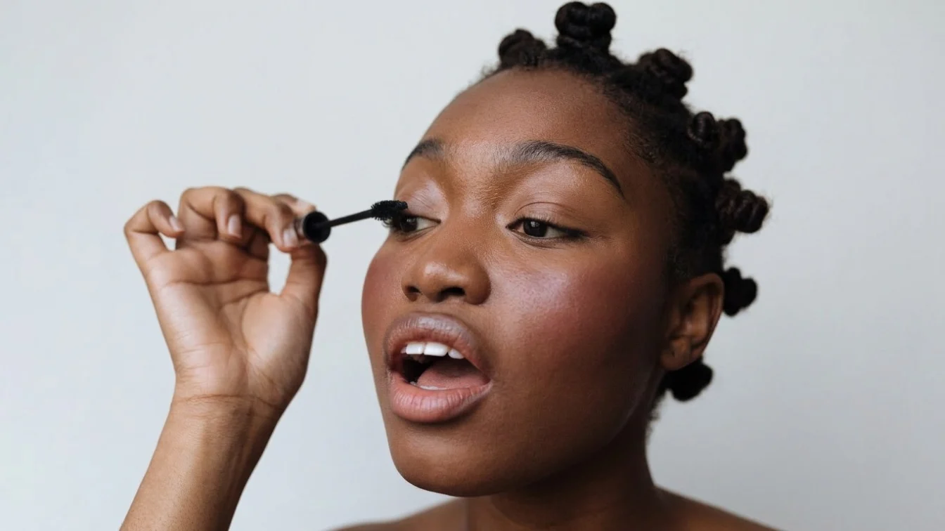 A woman applies mascara to her eyelashes.