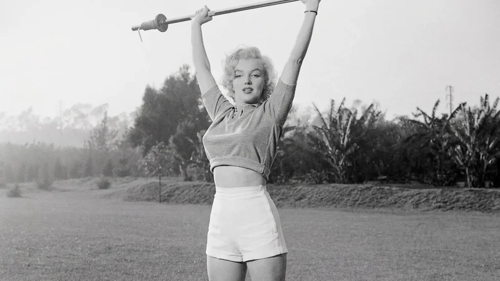 Marilyn Monroe reaching for the sky on tiptoe holding a light barbell.