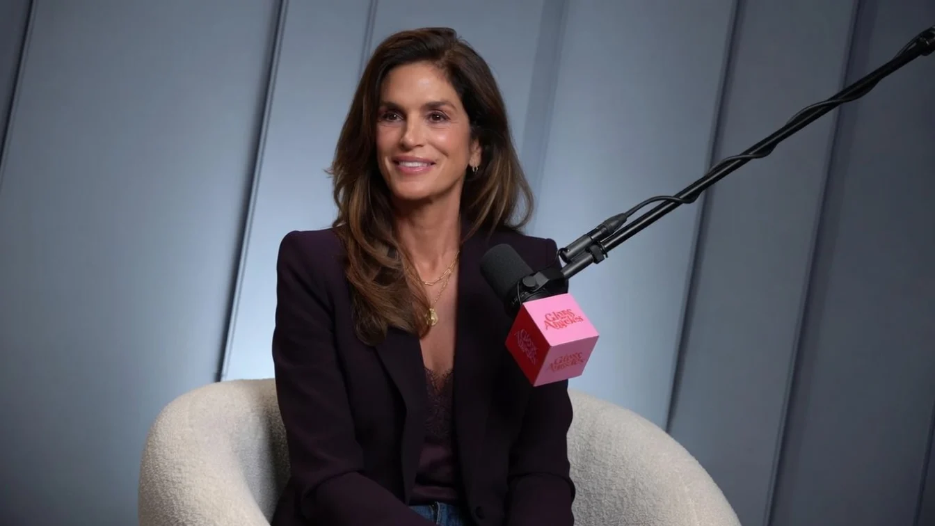Cindy Crawford wearing a blazer and sitting behind a microphone